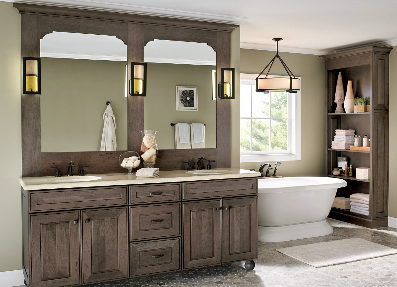 Grey-brown mitred-panel double vanity with a full arched mirror surround, bun feet and paired dark faucets, with a matching tall linen cabinet and a freestanding tub to the right
