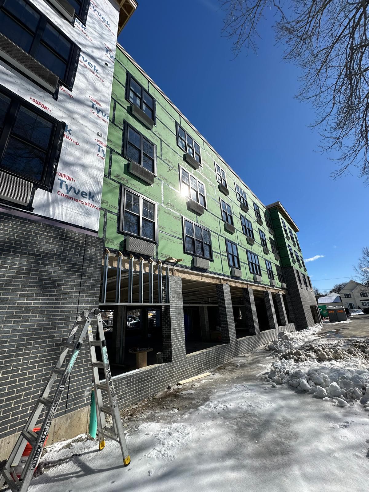 Green sheathed facade with black windows over a gray brick podium